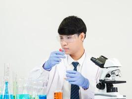 Porträt asiatisch Mann Schüler Wissenschaftler tragen ein Arzt Kleid im das Labor suchen Hand beim Chemiker. verursacht durch Mischen Reagenzien im wissenschaftlich Forschung Laboratorien mit Prüfung Röhren und Mikroskop auf das Tabelle foto