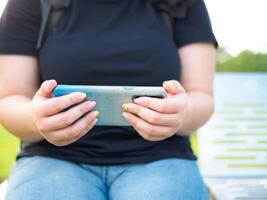 schließen oben Hand jung Frau asiatisch mollig süß schön einer Person Sitzung aussehen halten verwenden spielen Clever Telefon im Garten Park draussen Abend Sonnenlicht frisch lächelnd heiter glücklich entspannen Sommer- Tag foto