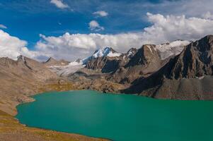 Alakel, ein heiter Türkis See, ist umarmt durch hoch aufragend, robust Berge mit schneebedeckt Spitzen, unter ein riesig und öffnen Blau Himmel, reflektieren der Natur unberührt Pracht im das Hochland foto