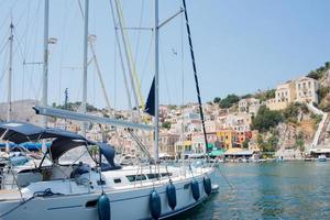 weiße Yacht, die an einem sonnigen Tag zum bunten Hafen von Symi ankommt. Griechenland. foto