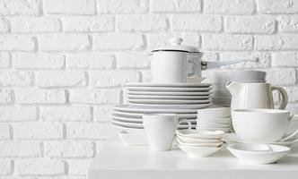 Stapel weißes keramisches Geschirr und Geschirr auf dem Tisch auf weißem Backsteinmauerhintergrund foto