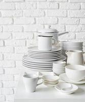 Haufen von weißem Keramikgeschirr und Geschirr auf dem Tisch auf weißem Backsteinmauerhintergrund