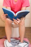 jung Frauen lesen ein Buch während Sitzung im das Toilette. foto