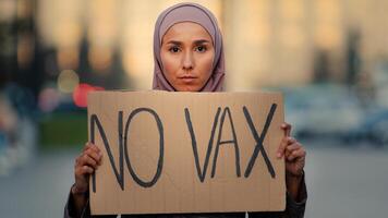 Porträt weiblich Muslim islamisch Mädchen Frau im Hijab Stehen im Stadt draußen zeigen Karton Banner Zeichen Text Nein vax Protest gegen Immunisierung covid19 Coronavirus Impfung Impfstoff Verweigerung foto