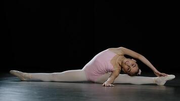 Teenager motiviert flexibel Fachmann Akrobat Ballerina Tänzer Mädchen Kind Sitzung auf Fußboden auf spaltet sich Schnur gelehnt zu Seite Dehnen üben akrobatisch Gymnastik- Elemente Ausbildung im tanzen Klasse foto