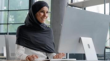 jung arabisch Geschäftsfrau im Hijab Arbeiten auf Computer lächelnd genießen Büro Arbeit erfolgreich Frau Fachmann Manager Unternehmen Mitarbeiter entwickelt Projekt online suchen zum Information auf Internet foto