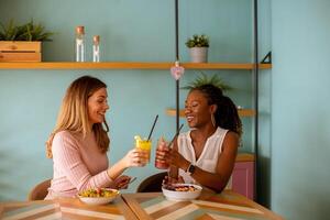 jung schwarz und kaukasisch Frau haben gut Zeit, Trinken frisch Säfte und haben gesund Frühstück im das Cafe foto