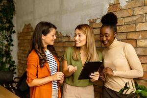 drei jung Geschäft Frauen mit Digital Tablette Stehen durch das Backstein Mauer im das industriell Stil Büro foto