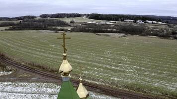 Initiale Winter. Clipansicht von ein Drohne auf ein Landschaft mit schneebedeckt Gras im ein Feld wo Dort ist ein Tempel mit ein golden Kreuz auf ein golden Kuppel gegen das Blau Himmel. foto