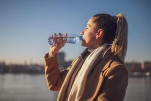 Frau genießt Trinken Wasser während Sitzung durch das Fluss auf ein sonnig Winter Tag. getönt Bild. foto