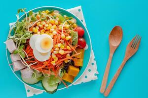 frisch Salat Gemüse mit gekocht Hähnchen Ei, hölzern Löffel und Gabel auf Blau Hintergrund foto