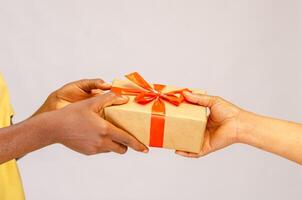 Urlaub Feier Konzept. Nahansicht auf weiblich Hände halten Geschenk mit rot Bogen und geben Geschenk Box zu afrikanisch amerikanisch Frau, Gruß mit Geburtstag, Weihnachten und Neu Jahr beim Zuhause foto