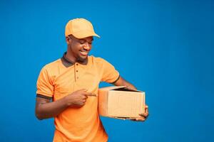 gut aussehend afrikanisch Kerl Gefühl aufgeregt wie er Punkte zu das Lieferung Paket auf seine Hand foto