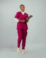 Porträt von ein jung heiter afrikanisch Frau tragen Gesundheit Uniform halten Bücher. foto