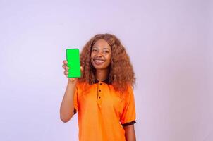 schön schwarz Mädchen zeigt an ihr Telefon Bildschirm während Gefühl glücklich und aufgeregt, Werbung Konzept, Fokus auf ihr Gesicht foto