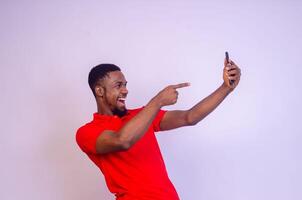 gut aussehend jung afrikanisch Mann zeigen zu seine Telefon Bildschirm im Aufregung foto