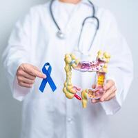 Arzt halten Blau Band mit Mensch Doppelpunkt Anatomie Modell. März kolorektal Krebs Bewusstsein Monat, Dickdarm Krankheit, groß Darm, Geschwür Kolitis, Verdauungs- System und Gesundheit Konzept foto