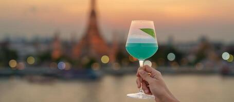 Tourist Hand zeigt an Cocktail Glas während genießen Aussicht zu wat arun Tempel im Sonnenuntergang, Reisender besucht Tempel von Dämmerung in der Nähe von von Dach Bar. Reise Ziel im Bangkok, Thailand und Süd-Ost Asien foto