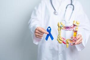 Arzt halten Blau Band mit Mensch Doppelpunkt Anatomie Modell. März kolorektal Krebs Bewusstsein Monat, Dickdarm Krankheit, groß Darm, Geschwür Kolitis, Verdauungs- System und Gesundheit Konzept foto