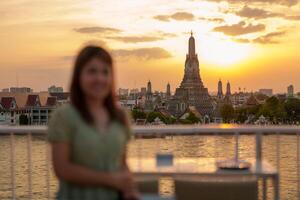 Tourist Frau genießt Aussicht zu wat arun Tempel im Sonnenuntergang, Reisender besucht Tempel von Dämmerung in der Nähe von Chao Phraya Fluss von Dach Bar. Wahrzeichen und Reise Ziel im Bangkok, Thailand und Süd-Ost Asien foto