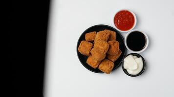 gebraten Tofu auf ein schwarz Teller mit drei Saucen von Mayonnaise, Chili und Süss Soja Soße auf ein Weiß Hintergrund foto