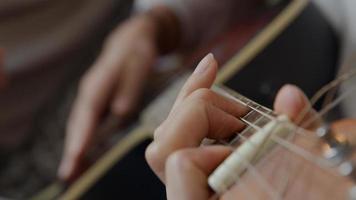 Nahaufnahme der Hand der jungen Mischlingsfrau, die Stimmgeräte auf Spindelstock der Gitarre einstellt foto