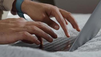 Nahaufnahme von Laptop auf Bett und Händen des jungen Mannes aus dem Nahen Osten, Scrollen auf Touchpad und Eingabe der Tastatur foto