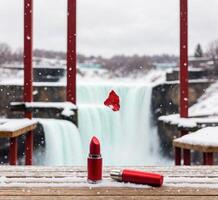 ai generiert rot Lippenstift auf ein hölzern Tabelle im Vorderseite von ein Wasserfall und fallen Schnee foto