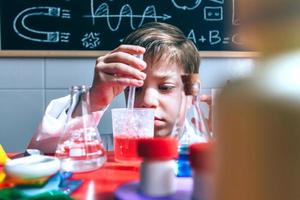 Kind spielt mit chemischen Flüssigkeiten über Tisch foto