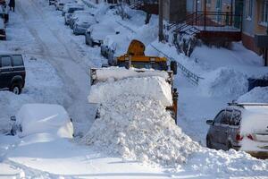 traktor, der am wintertag schnee vom parkplatz in der nähe des wohngebäudes entfernt foto