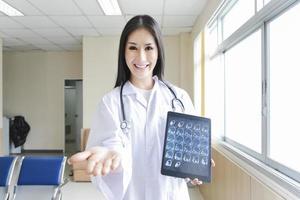 Porträt einer intelligenten Ärztin, die ein Tablet hält, um ein Röntgenbild zu zeigen und an der Rezeption des Krankenhauses steht. foto