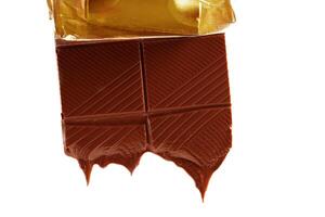 Stück von geschmolzen Schokolade Bar im golden Verpackung isoliert auf Weiß Hintergrund. Schokolade tropft. foto