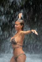 schön jung Frau entspannt sich unter ein Wasserfall. sexy Mädchen im ein Bikini posieren in der Nähe von ein Wasserfall im das Tropen. foto