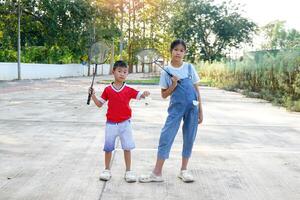 asiatisch Mädchen und Junge abspielen Badminton draußen beim das Park zusammen auf Urlaub. Sanft und selektiv Fokus. foto