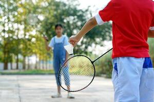 asiatisch Mädchen und Junge abspielen Badminton draußen beim das Park zusammen auf Urlaub. Sanft und selektiv Fokus. foto