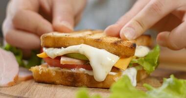 Herstellung ein Sandwich mit Schinken, Salat, reif Tomate Scheiben und Stücke von Käse. schnell Essen Konzept. foto