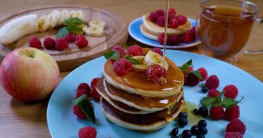 Süss Honig Gießen Über Pfannkuchen. lecker Frühstück Lebensmittel. Pfannkuchen sind serviert mit Himbeeren, Banane und Minze Blatt. Honig tropft Nieder auf Dessert foto