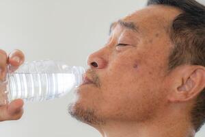 Glück von männlich Alten halten ein Flasche von Wasser. Senior Menschen Trinken frisch Mineral Wasser. foto