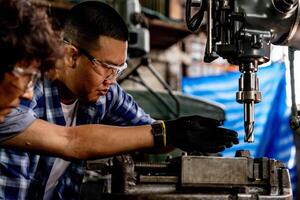 asiatisch Arbeiter im Produktion Pflanze Bohren beim Maschine. Fachmann Arbeiter in der Nähe von Bohren Maschine auf Fabrik. Fertigstellung Metall Arbeiten intern Stahl Oberfläche auf Drehbank Schleifer Maschine mit fliegend Funken. foto