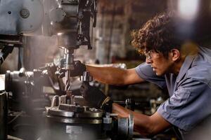 asiatisch Arbeiter im Produktion Pflanze Bohren beim Maschine. Fachmann Arbeiter in der Nähe von Bohren Maschine auf Fabrik. Fertigstellung Metall Arbeiten intern Stahl Oberfläche auf Drehbank Schleifer Maschine mit fliegend Funken. foto