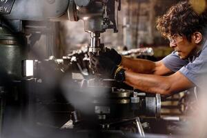 asiatisch Arbeiter im Produktion Pflanze Bohren beim Maschine. Fachmann Arbeiter in der Nähe von Bohren Maschine auf Fabrik. Fertigstellung Metall Arbeiten intern Stahl Oberfläche auf Drehbank Schleifer Maschine mit fliegend Funken. foto