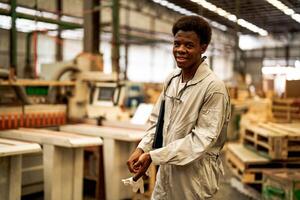 afrikanisch Mann Arbeitskräfte Ingenieurwesen Stehen mit Vertrauen mit Arbeiten Suite Kleid und Hand Handschuh im Vorderseite Maschine. Konzept von Clever Industrie Arbeiter Betriebs. Holz Fabrik produzieren Holz Gaumen. foto