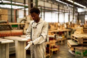 afrikanisch Mann Arbeitskräfte Ingenieurwesen Stehen mit Vertrauen mit Arbeiten Suite Kleid und Hand Handschuh im Vorderseite Maschine. Konzept von Clever Industrie Arbeiter Betriebs. Holz Fabrik produzieren Holz Gaumen. foto