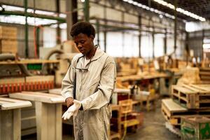 afrikanisch Mann Arbeitskräfte Ingenieurwesen Stehen mit Vertrauen mit Arbeiten Suite Kleid und Hand Handschuh im Vorderseite Maschine. Konzept von Clever Industrie Arbeiter Betriebs. Holz Fabrik produzieren Holz Gaumen. foto