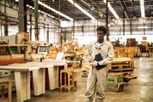 afrikanisch Mann Arbeitskräfte Ingenieurwesen Stehen mit Vertrauen mit Arbeiten Suite Kleid und Hand Handschuh im Vorderseite Maschine. Konzept von Clever Industrie Arbeiter Betriebs. Holz Fabrik produzieren Holz Gaumen. foto