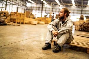 Mann Arbeitskräfte Ingenieurwesen Sitzung mit Vertrauen mit Arbeiten Suite Kleid und Hand Handschuh im Vorderseite Maschine. Konzept von Clever Industrie Arbeiter Betriebs. Holz Fabrik produzieren Holz Gaumen. foto