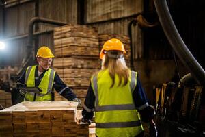 Mannschaft Arbeiter Zimmermann tragen Sicherheit Uniform und schwer Hut Arbeiten und Überprüfung das Qualität von hölzern Produkte beim Werkstatt Herstellung. Mann und Frau Arbeitskräfte Holz im dunkel Warenhaus Industrie. foto