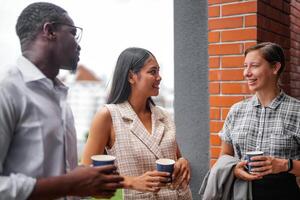 Mannschaft von Geschäft Menschen Clever Mann und Frauen Stand beim draussen Terrasse Gebäude und sich unterhalten zusammen mit Frühstück Essen und Kaffee auf das Hand im gut Gefühl mit Stadt Raum Gebäude. Geschäft Morgen. foto