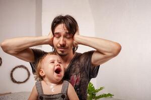 das Kind ist schreiend, hysterisch. ein müde Papa nicht wollen zu hören das Baby. das Elternteil ist irritiert, müde, will zu nehmen ein brechen von seine Tochter. Kinder- Hysterie. foto