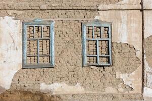 alt Haus Adobe Luft Backstein Mauer mit zwei eingebettet hölzern Fenster Frames und geschält aus Gips Reste - - eben Textur und voll Rahmen Hintergrund foto